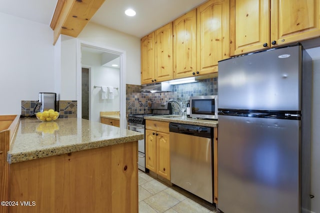 kitchen featuring appliances with stainless steel finishes, light brown cabinetry, sink, decorative backsplash, and light stone counters