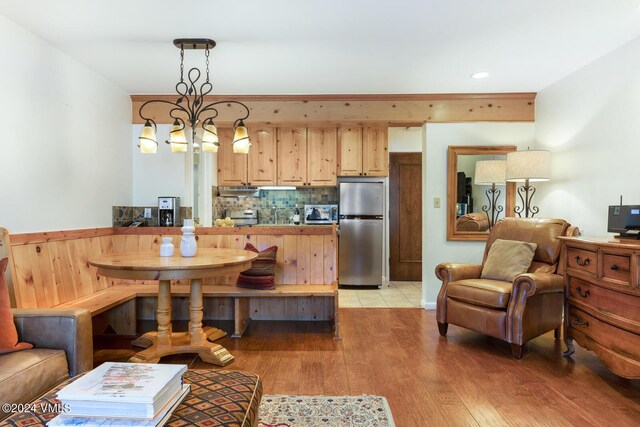 kitchen featuring pendant lighting, light brown cabinetry, stainless steel refrigerator, backsplash, and light hardwood / wood-style flooring