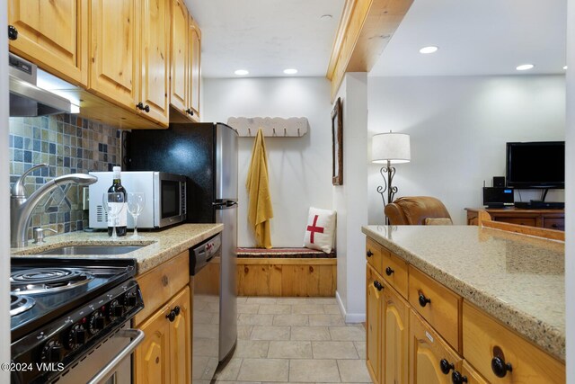 kitchen featuring tasteful backsplash, appliances with stainless steel finishes, light stone countertops, and sink