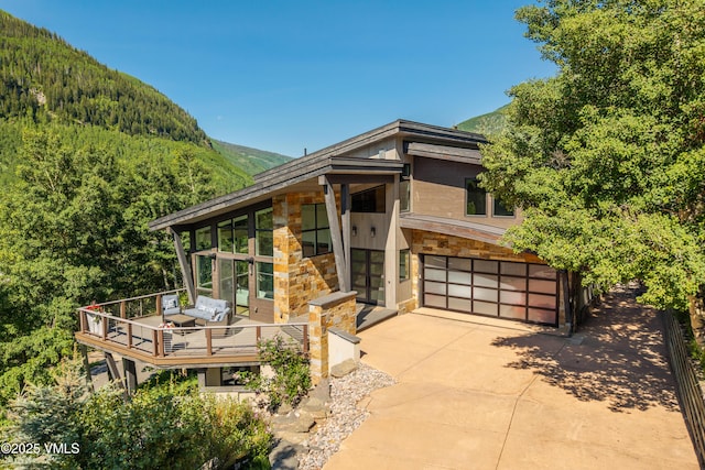 3235 Katsos Ranch Rd, Vail, CO 81657 - contemporary home featuring a garage, driveway, a forest view, stone siding, and a deck with mountain view