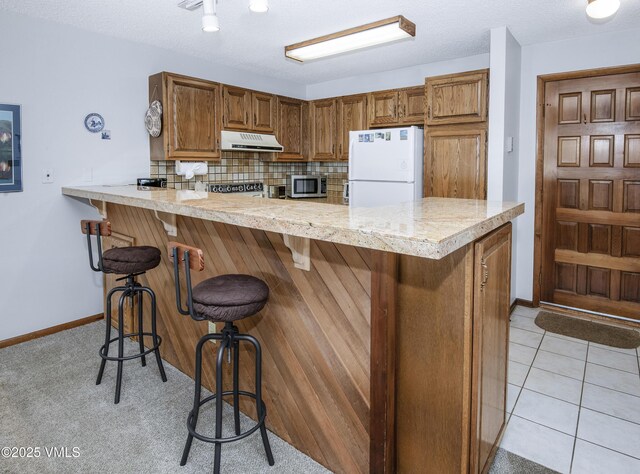 760 W Beaver Creek Blvd Unit 115, Avon, CO 81620 - kitchen with freestanding refrigerator, stainless steel microwave, range hood, a peninsula, and brown cabinetry