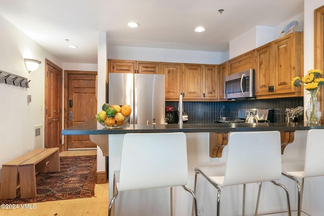 kitchen with kitchen peninsula, stainless steel appliances, light hardwood / wood-style flooring, tasteful backsplash, and a breakfast bar area