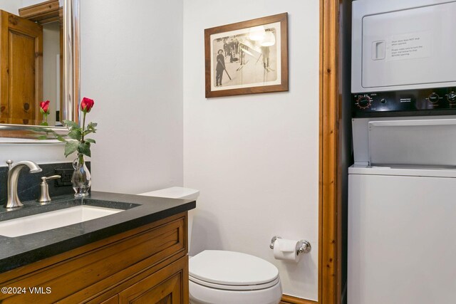 bathroom featuring toilet, vanity, and stacked washer and clothes dryer