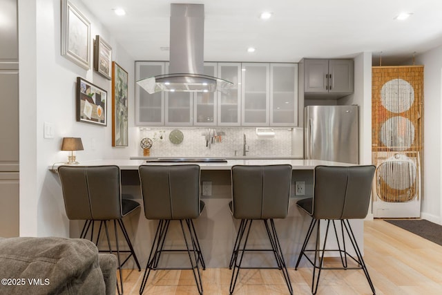 2783 Kinnikinnick Rd Unit 7, Vail, CO 81657 - kitchen with freestanding refrigerator, a breakfast bar area, gray cabinets, glass insert cabinets, and island range hood