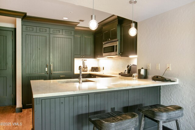 130 Daybreak Rdg Unit 732, Avon, CO 81620 - kitchen with green cabinetry, stainless steel microwave, a sink, a peninsula, and a textured wall