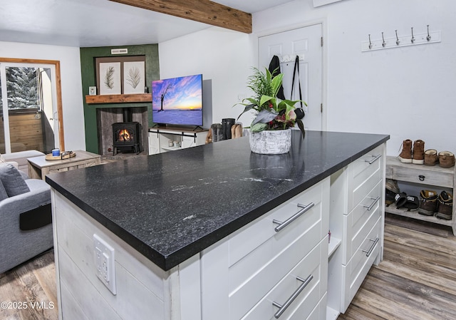 kitchen featuring white cabinetry, hardwood / wood-style flooring, a wood stove, beamed ceiling, and a large island