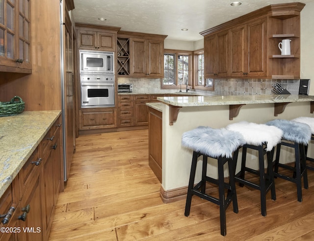 1120 Village Rd Unit 7, Beaver Creek, CO 81620 - kitchen featuring open shelves, stainless steel appliances, a breakfast bar, light wood-style floors, and brown cabinets