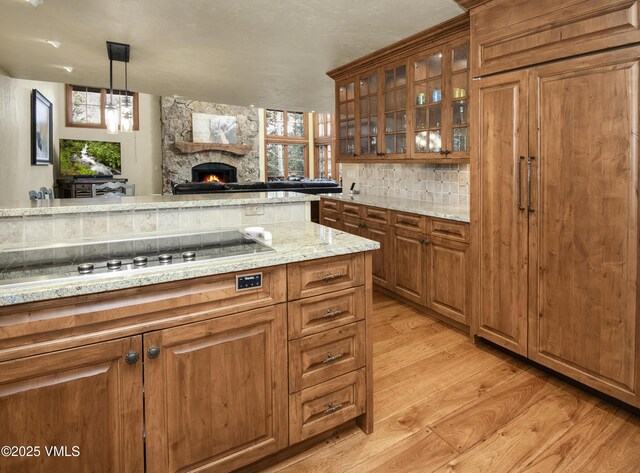 1120 Village Rd Unit 7, Beaver Creek, CO 81620 - kitchen with black electric cooktop, backsplash, light wood-style flooring, a stone fireplace, and brown cabinets