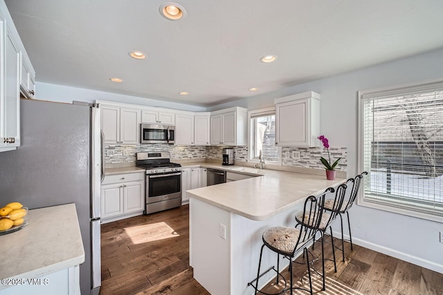 kitchen with tasteful backsplash, light countertops, appliances with stainless steel finishes, white cabinetry, and a peninsula