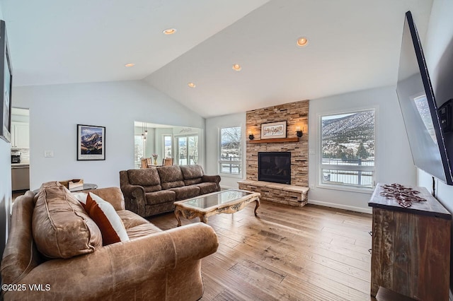 living area featuring recessed lighting, vaulted ceiling, a stone fireplace, light wood-type flooring, and baseboards