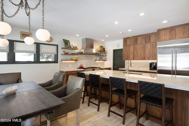 kitchen featuring a breakfast bar, island range hood, sink, hanging light fixtures, and stainless steel built in fridge