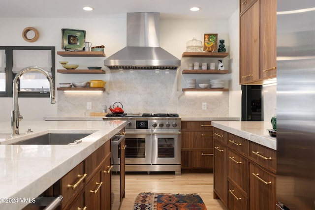 kitchen with appliances with stainless steel finishes, range hood, sink, light stone countertops, and light wood-type flooring