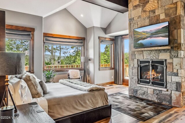 bedroom with lofted ceiling, a stone fireplace, multiple windows, and hardwood / wood-style flooring