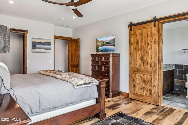 bedroom with connected bathroom, hardwood / wood-style floors, a barn door, and ceiling fan