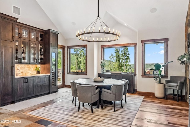 dining space with sink, a notable chandelier, light hardwood / wood-style flooring, and high vaulted ceiling