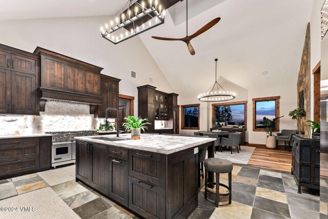 kitchen with sink, premium range hood, a kitchen island with sink, double oven range, and dark brown cabinetry