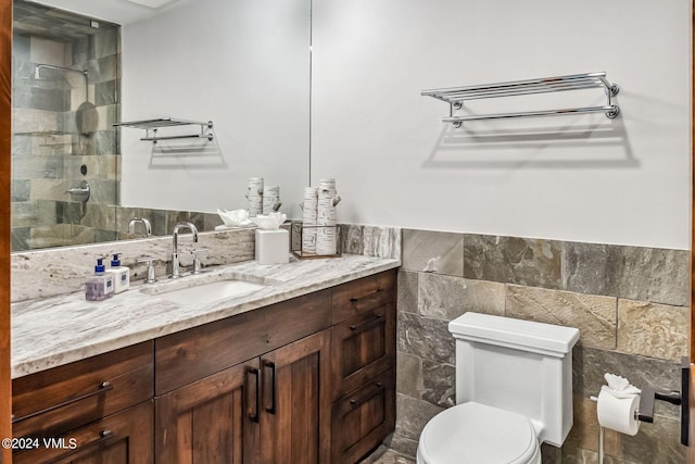 bathroom featuring vanity, a tile shower, tile walls, and toilet