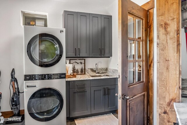 laundry area featuring cabinets, stacked washer and clothes dryer, and sink