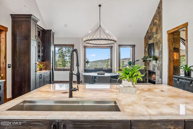 kitchen featuring dark brown cabinetry, sink, an inviting chandelier, decorative light fixtures, and vaulted ceiling