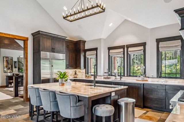 kitchen with a kitchen island, stainless steel built in refrigerator, sink, light stone countertops, and dark brown cabinets