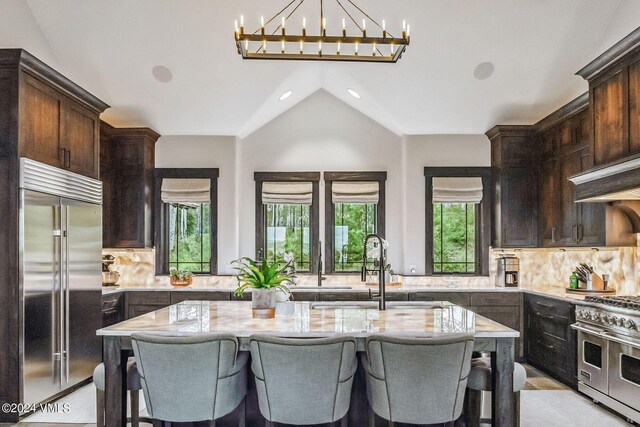 kitchen with high end appliances, decorative backsplash, light stone countertops, and an island with sink