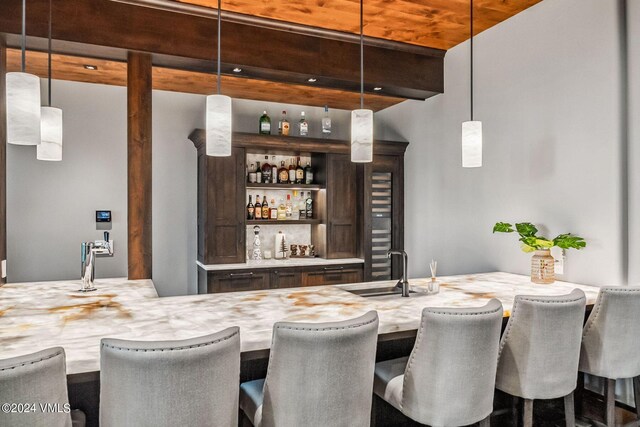 bar with beamed ceiling, dark brown cabinets, sink, and decorative light fixtures