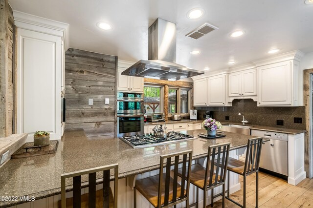 kitchen with appliances with stainless steel finishes, a breakfast bar, sink, white cabinets, and island exhaust hood