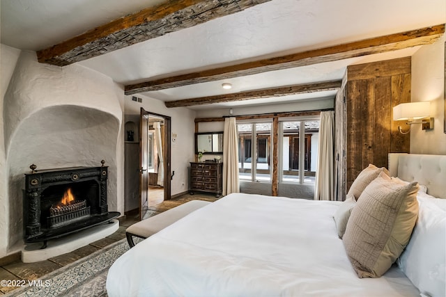 bedroom with a fireplace, beam ceiling, and access to outside