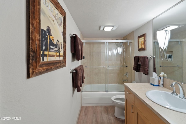 full bathroom featuring combined bath / shower with glass door, wood-type flooring, vanity, toilet, and a textured ceiling