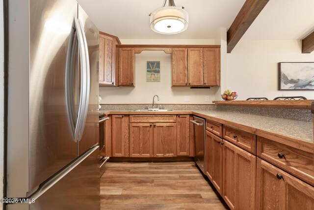 kitchen with appliances with stainless steel finishes, sink, beam ceiling, and light wood-type flooring