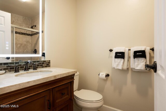 bathroom with vanity, backsplash, a shower with door, and toilet