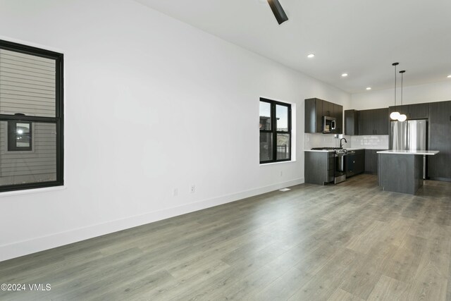 kitchen featuring hanging light fixtures, a center island, dark brown cabinetry, stainless steel appliances, and light wood-type flooring