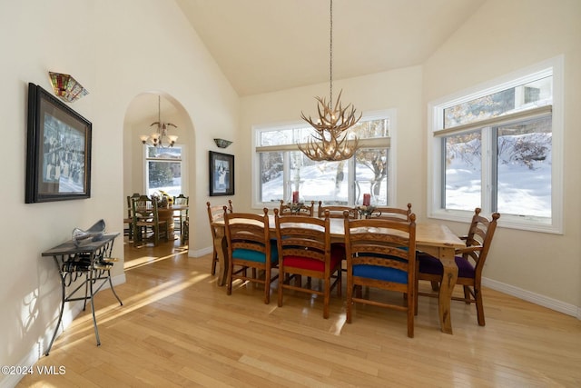 dining area with a notable chandelier, light hardwood / wood-style flooring, and high vaulted ceiling