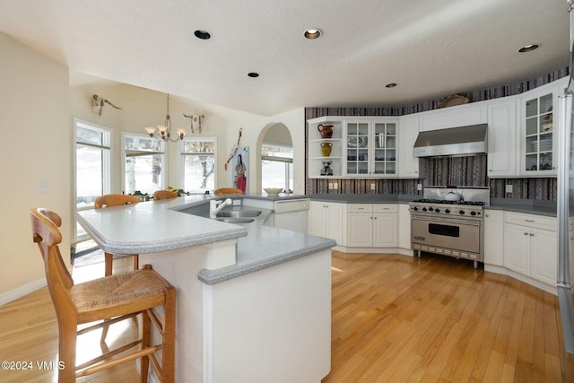 kitchen with white cabinetry, hanging light fixtures, premium stove, a kitchen bar, and wall chimney exhaust hood