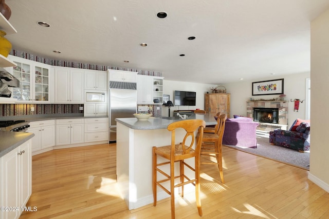 kitchen with a kitchen breakfast bar, built in appliances, a fireplace, white cabinets, and light wood-type flooring