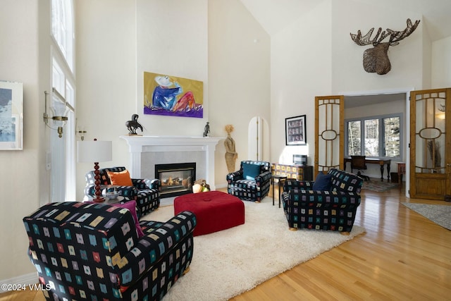 living room with a tiled fireplace, a towering ceiling, and wood-type flooring