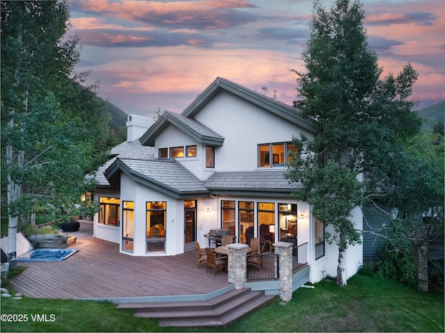 4465 Glen Falls Ln, Vail, CO 81657 - back of property at dusk featuring stucco siding, a deck, a lawn, and a chimney