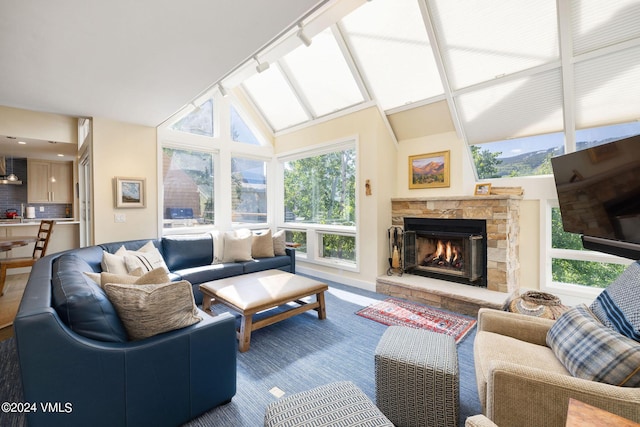 living room with rail lighting, vaulted ceiling, a fireplace, and plenty of natural light