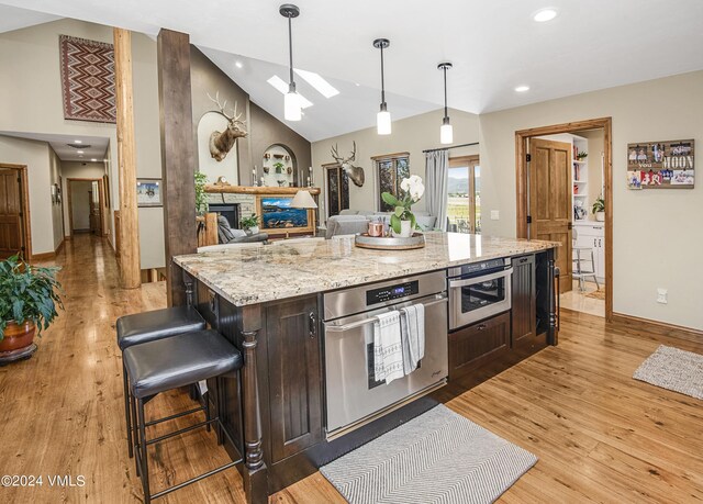 kitchen with hanging light fixtures, a kitchen island, dark brown cabinets, and light hardwood / wood-style floors