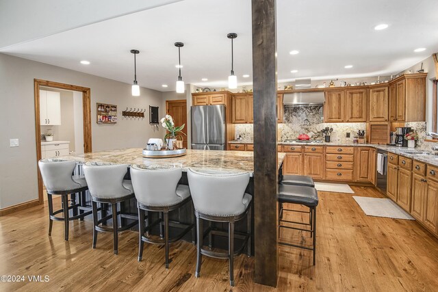 kitchen featuring wall chimney range hood, stainless steel appliances, a breakfast bar, and a spacious island