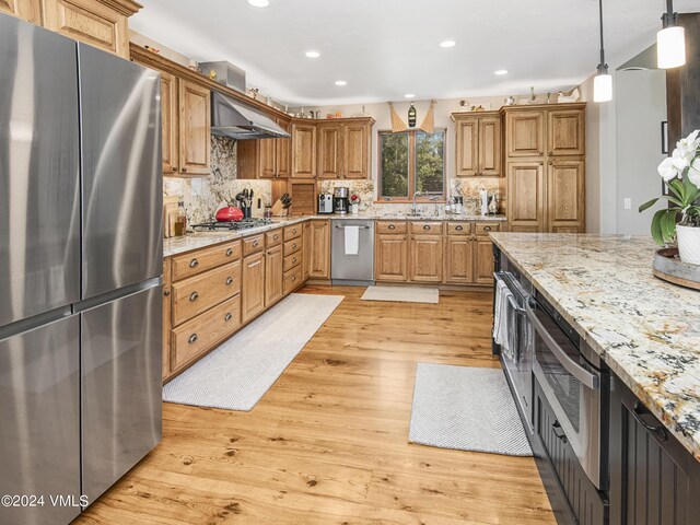 kitchen with sink, range hood, stainless steel appliances, light stone countertops, and light wood-type flooring