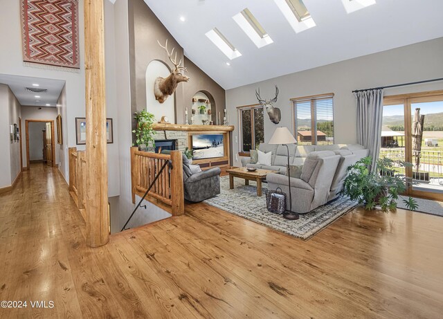 living room featuring wood-type flooring, a fireplace, a skylight, and high vaulted ceiling