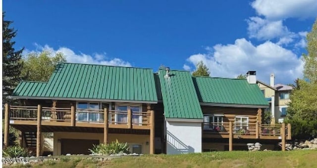 rear view of house featuring a chimney, stucco siding, a standing seam roof, metal roof, and a garage