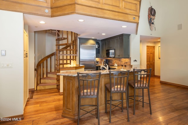 kitchen featuring decorative backsplash, appliances with stainless steel finishes, a peninsula, and light wood-style floors