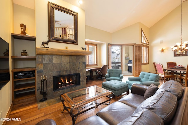 living room with an inviting chandelier, wood finished floors, a tiled fireplace, and vaulted ceiling