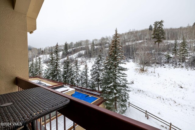 snow covered back of property featuring a wooded view