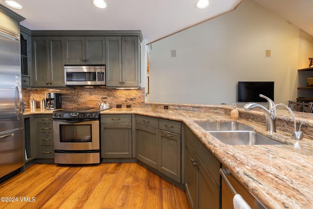 kitchen with light stone countertops, a sink, stainless steel appliances, light wood-type flooring, and backsplash