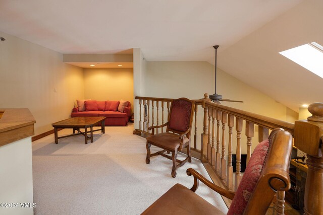 carpeted living room with baseboards, vaulted ceiling with skylight, and a ceiling fan