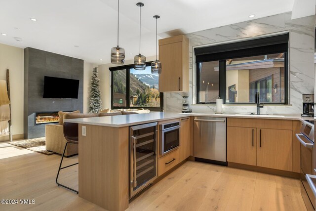 kitchen featuring wine cooler, sink, appliances with stainless steel finishes, kitchen peninsula, and pendant lighting