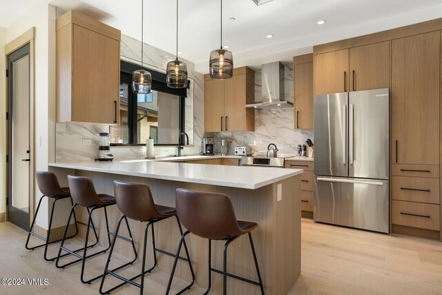 kitchen with tasteful backsplash, a kitchen breakfast bar, pendant lighting, stainless steel appliances, and wall chimney range hood